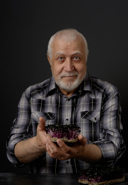 Un agricultor adulto de pelo gris, de edad, muestra la cosecha de microvegetales en sus manos