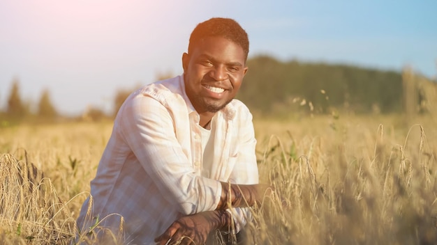 Agricultor afro-americano senta-se no campo de trigo sorrindo