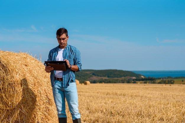 agricultor agrônomo masculino com um tablet em jeans azul e camisa e camiseta branca em campo com palheiros