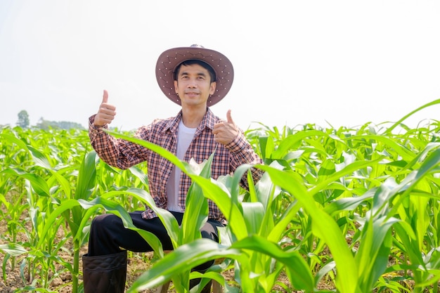 Agricultor asiático con camisa a rayas y sombrero sentado en la granja de maíz