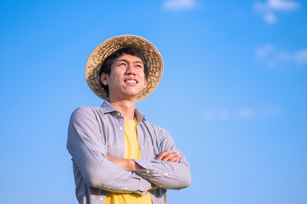 Agricultor asiático cruza os braços e sorri com o céu azul