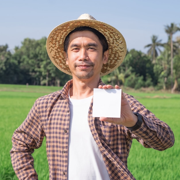 Agricultor asiático em pé segurando um papel em branco em uma fazenda