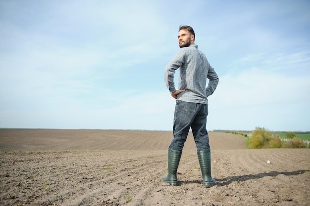 Un agricultor con botas trabaja en un campo sembrado en primavera Un agrónomo camina por la tierra evaluando un campo arado en otoño Agricultura