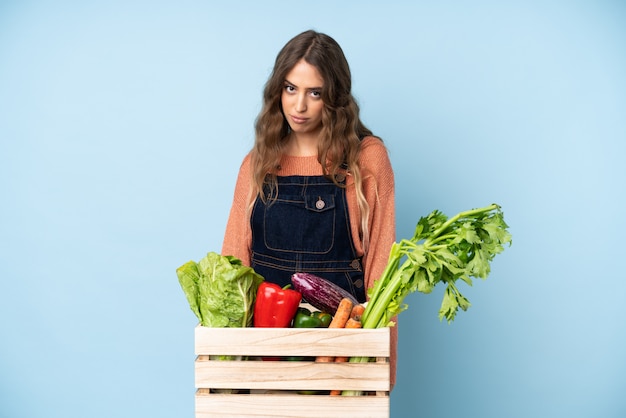 Agricultor com legumes recém colhidos em uma caixa com expressão triste e deprimida