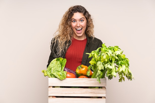 Agricultor com legumes recém colhidos em uma caixa em bege com expressão facial de surpresa