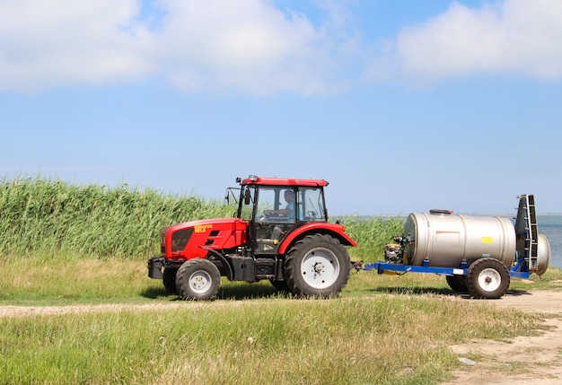 Un agricultor conduce un tractor con un rociador conectado a lo largo de la bahía y cañas Agricultura
