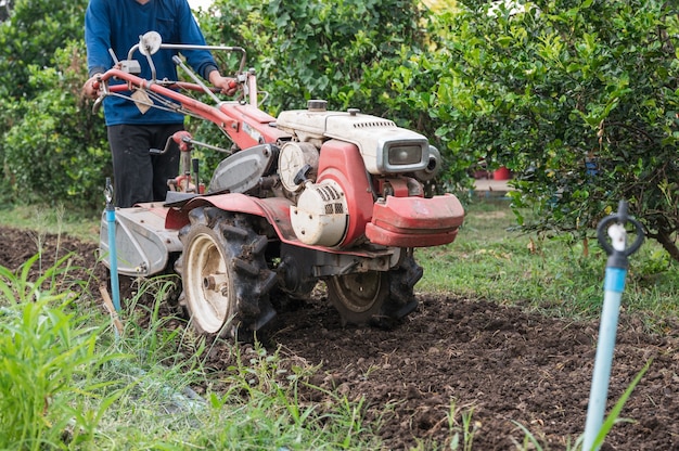 Agricultor controlando trator de duas rodas arando no campo de solo na plantação