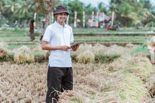 El agricultor dueño del campo de arroz sonríe mientras está de pie sosteniendo la almohadilla en el campo de arroz