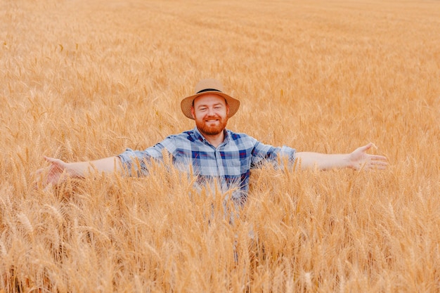 Un agricultor feliz con los brazos extendidos de pie en su campo de semillas de trigo en crecimiento