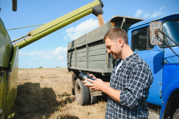 Agricultor feliz orgulhosamente em um campo Motorista de colheitadeira indo para colheita de trigo rico Agrônomo vestindo camisa de flanela olhando para a câmera em uma terra