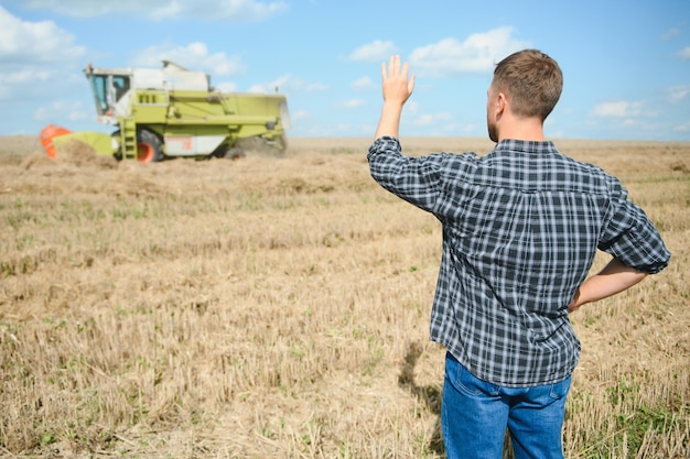 Agricultor feliz orgulhosamente em um campo motorista de colheitadeira indo para colheita de trigo rico agrônomo vestindo camisa de flanela olhando para a câmera em uma terra