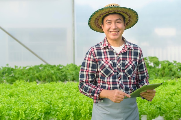 Un agricultor feliz trabajando con tableta en la granja de invernadero hidropónico