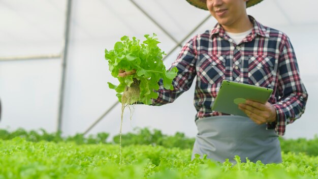 Un agricultor feliz trabajando con tableta en la granja de invernadero hidropónico