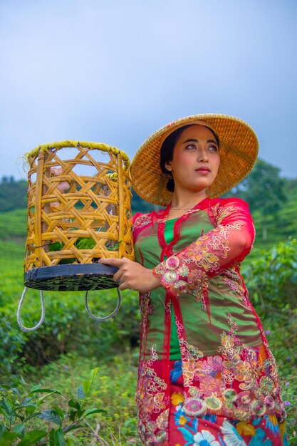 Foto un agricultor de hojas de té posando con una cesta de bambú en sus manos temprano en la mañana