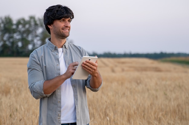 Agricultor homem usando computador tablet digital em um campo de trigo e usando aplicativos e verificando quali ...