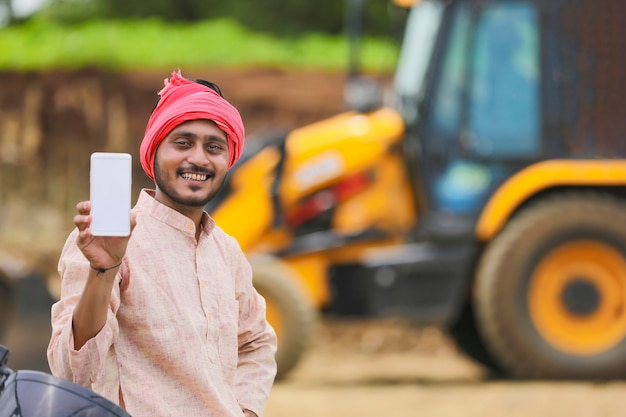 Agricultor indiano mostrando smartphone com seu novo equipamento de máquina de movimentação de terras