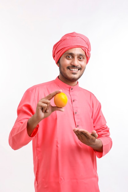 Agricultor indiano segurando uma fruta laranja na mão sobre fundo branco.