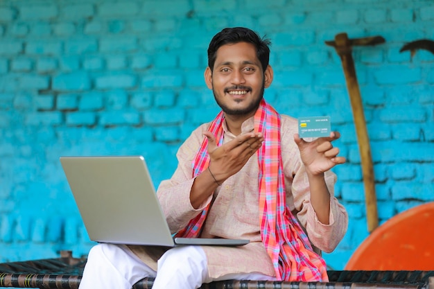 Foto agricultor indiano usando laptop e cartão em casa.