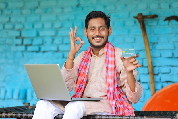 Agricultor indiano usando laptop e cartão em casa.