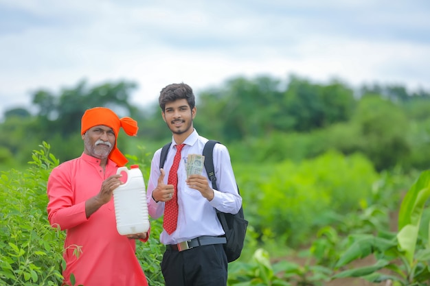 Agricultor indio con agrónomo en el campo, agricultor y agrónomo mostrando botella de fertilizante