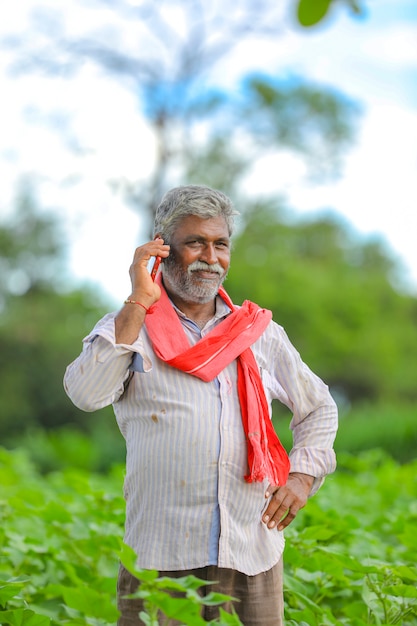 Agricultor indio hablando por teléfono móvil en el campo agrícola