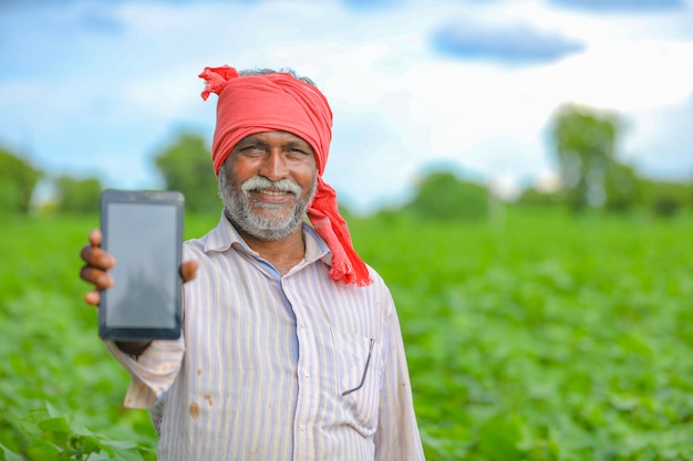 Agricultor indio mostrando una pantalla móvil en el campo agrícola