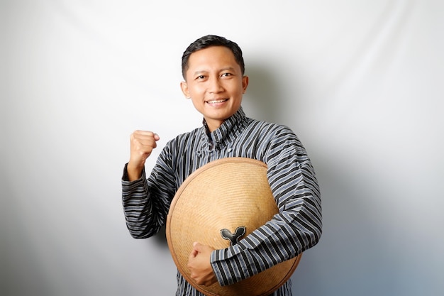 Foto agricultor indonésio vestindo lurik segurando um caping com a mão fechada isolado em fundo branco