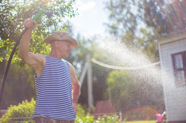 Agricultor con manguera de jardín y boquilla de arma regando plantas de verduras en verano Concepto de jardinería Plantas agrícolas que crecen en fila de cama