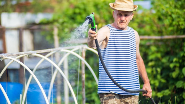 Agricultor con manguera de jardín y boquilla de arma regando plantas de verduras en verano Concepto de jardinería Plantas agrícolas que crecen en fila de cama