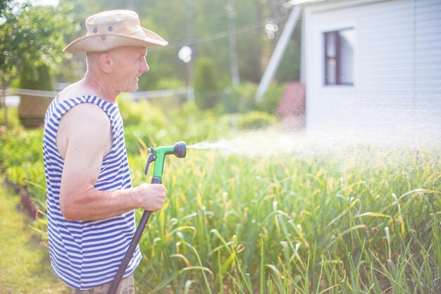 Agricultor con manguera de jardín y boquilla de arma regando plantas de verduras en verano Concepto de jardinería Plantas agrícolas que crecen en fila de cama