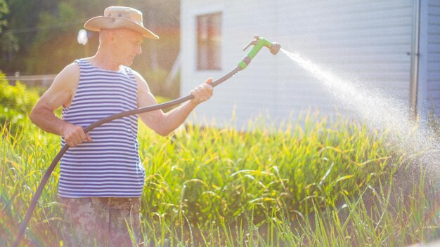 Agricultor con manguera de jardín y boquilla de arma regando plantas de verduras en verano Concepto de jardinería Plantas agrícolas que crecen en fila de cama