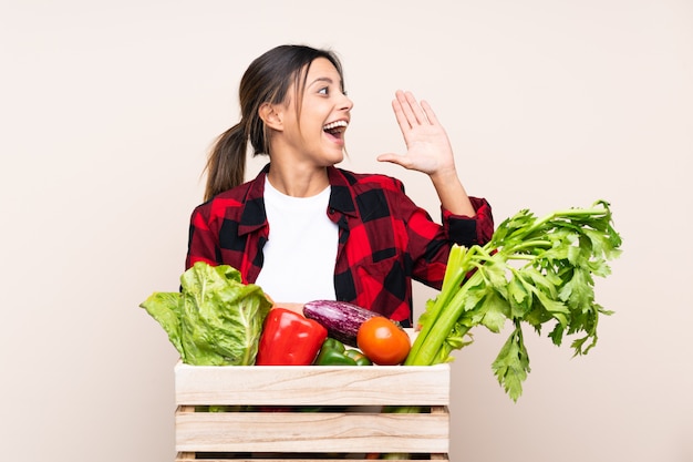 Foto agricultor mulher segurando legumes frescos em uma cesta de madeira, gritando com a boca aberta