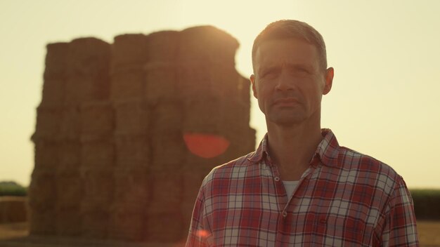 Agricultor posando fardos de heno en el retrato de la luz del sol Agrónomo enfocado inspeccionando