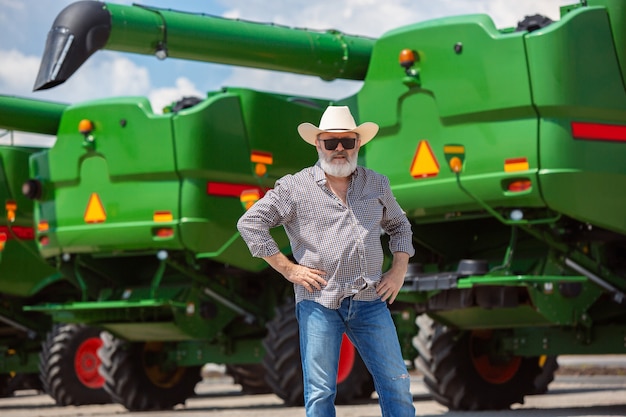 Agricultor profissional com um trator moderno, combine em um campo de luz solar no trabalho. Cores de verão confiantes e brilhantes. Agricultura, exposição, maquinaria, produção vegetal. Último homem perto de sua máquina.