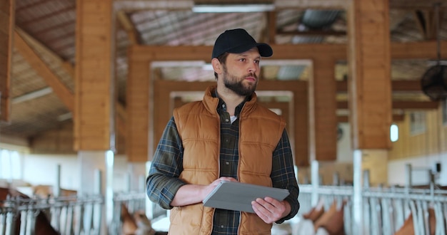 Agricultor que usa una computadora de tableta en una granja lechera moderna establo Propietario de agronegocios que verifica los datos sostienen una tableta en la cría de animales Establo granero establo interior establo