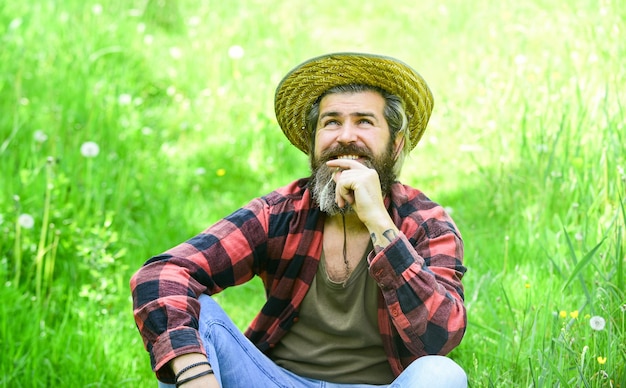 Agricultor relaxado com chapéu de palha. jardineiro homem maduro relaxe na grama verde. aproveite a natureza da primavera. a temporada de verão é perfeita. Hipster de rancho brutal usa camisa quadriculada. agricultura e agricultura. Vida Verde.