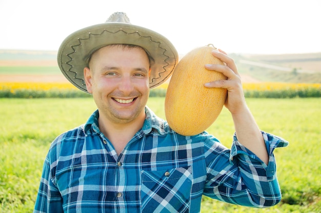 Agricultor satisfeito tem um melão no ombro o homem com o chapéu olhando para a câmera e segurando ...