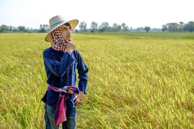 Agricultor tailandês em trajes tradicionais e touca em pé pensando no meio do campo