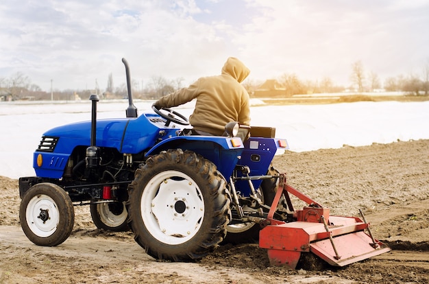 Agricultor en un tractor con fresadora afloja muele y mezcla tierra Aflojando la superficie