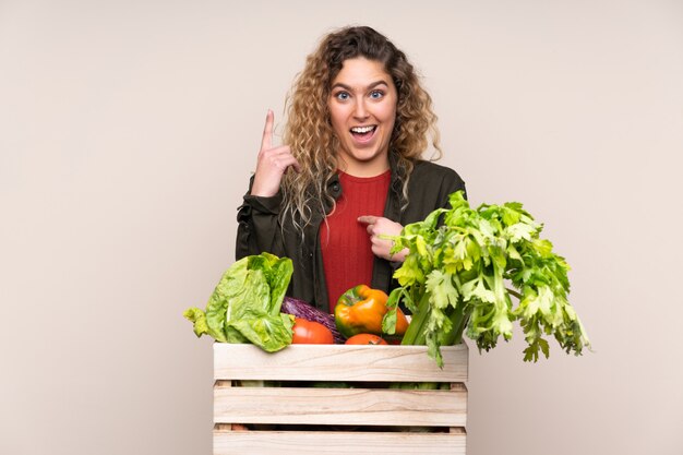 Agricultor con verduras recién cortadas en una caja aislada en la pared de color beige con expresión facial sorpresa