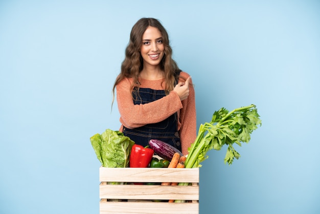 Agricultor con verduras recién cortadas en una caja apuntando hacia atrás