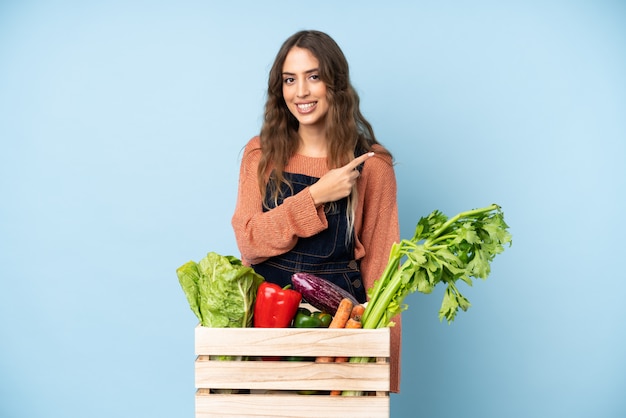 Agricultor con verduras recién cortadas en una caja apuntando hacia un lado para presentar un producto