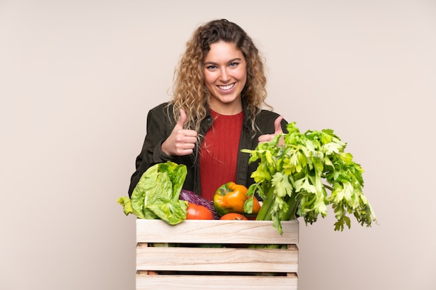 Agricultor con verduras recién cortadas en una caja en la pared de color beige dando un gesto de aprobación