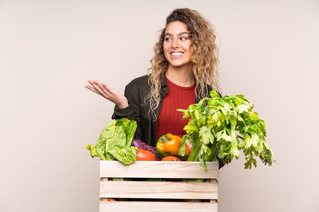 Agricultor con verduras recién cortadas en una caja en la pared de color beige con espacio en blanco imaginario en la palma