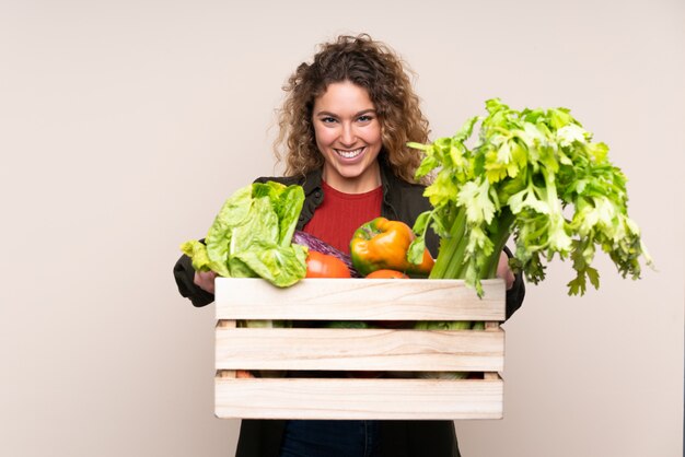 Agricultor con verduras recién cortadas en una caja en la pared de color beige