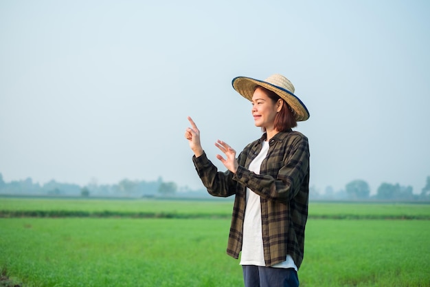 Foto agricultora asiática vestida con blusas marrones y vaqueros de pie y toca la pantalla en el aire