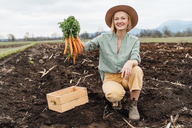 Agricultora con una caja de madera llena de verduras crudas frescas en un campo agrícola