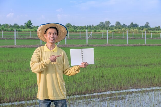 Los agricultores asiáticos visten de amarillo de pie y sosteniendo un cuaderno en la granja verde. Imagen para presentación.