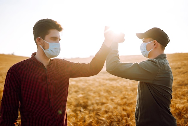 Agricultores com máscaras médicas estéreis no rosto cumprimentam seus cotovelos em um campo de trigo Pare de apertos de mão