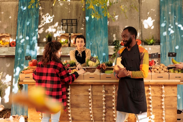 Agricultores e clientes felizes conversando sobre produtos bionaturais exibidos na banca do mercado de agricultores locais. Pessoas diversas e alegres que vendem produtos agrícolas e frutas ou vegetais orgânicos.